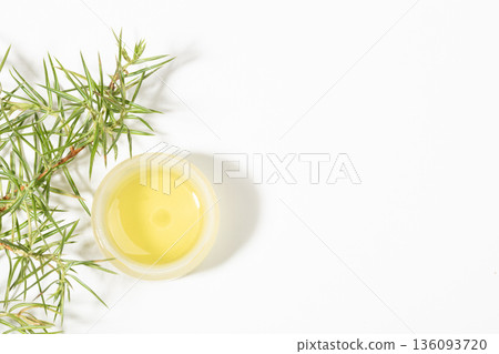 Top view to small round jar with essential juniper with fresh juniper leaves on white. Copy space 136093720