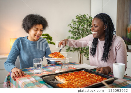 Mother serving pizza to daughter at home dinner 136093932