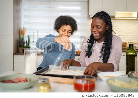 Black mother and daughter preparing homemade pizza together Black mother and daughter preparing homemade pizza together 136093942