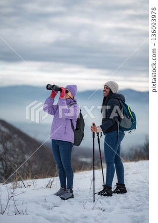 Friends exploring winter mountains with binoculars and hiking poles Friends exploring winter mountains with binoculars and hiking poles 136093978
