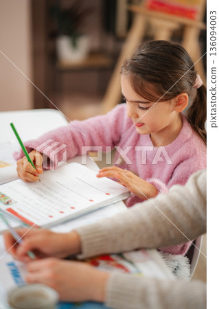 Young girl studying homework with adult helper 136094003