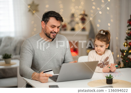 Father and daughter enjoying Christmas online shopping with laptop 136094022