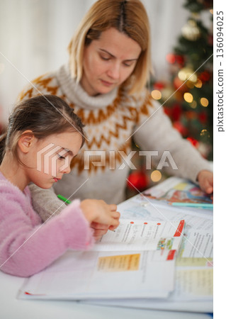 Mother helping daughter with homework near Christmas tree Mother helping daughter with homework near Christmas tree 136094025