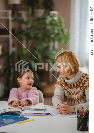 Mother and daughter learning together at home, smiling and doing homework Mother and daughter learning together at home, smiling and doing homework 136094043