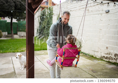 Father pushing daughter on swing, dog watching family bonding Father pushing daughter on swing, dog watching family bonding 136094070