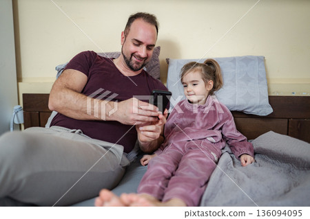 Father and daughter watching smartphone together in bed 136094095