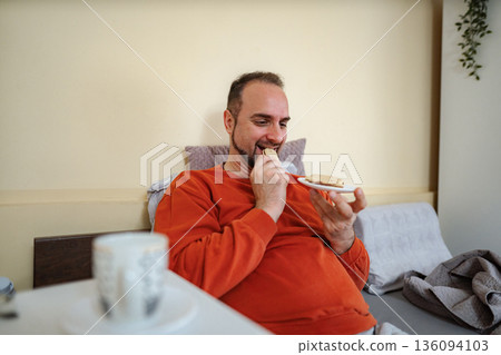 Man enjoying snack cookies in bed in morning Man enjoying snack cookies in bed in morning 136094103