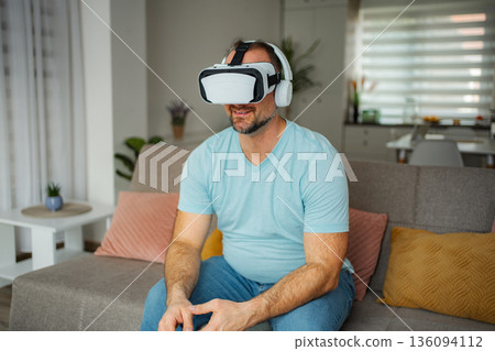 Man enjoying virtual reality headset on couch at home Man enjoying virtual reality headset on couch at home 136094112