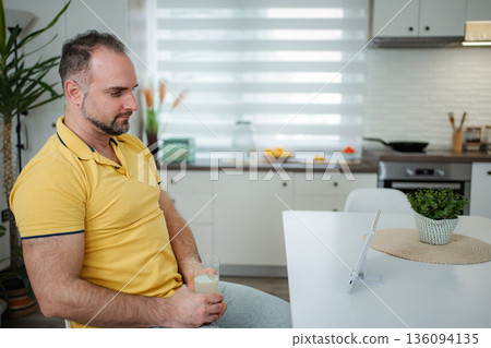 Mature adult man relaxing with healthy drink while looking at tablet 136094135