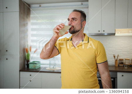 Mature adult man drinking healthy beverage in kitchen Mature adult man drinking healthy beverage in kitchen 136094158