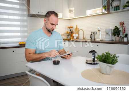 Man drinking coffee and using tablet in kitchen at home 136094162
