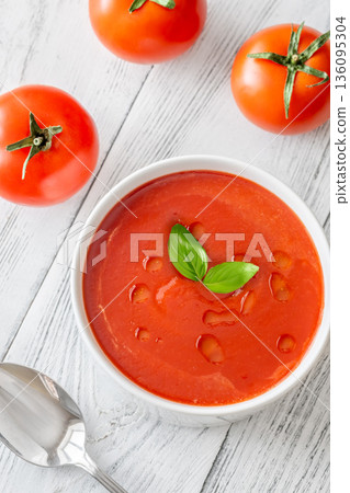 Minimal tomato soup with basil and olive oil on white wooden table 136095304