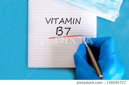 Vitamin B7 biotin symbol. Concept words Vitamin B7 on beautiful white note. Doctor's hand in blue medical glove. Medical mask. Beautiful blue background. Medical healthy lifestyle Vitamin B7 concept. 136095727