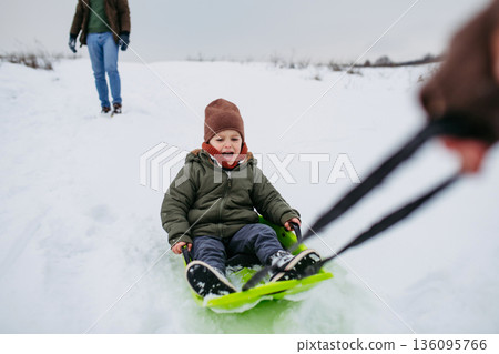 Dad and child bobbing downhill on snow slider. 136095766