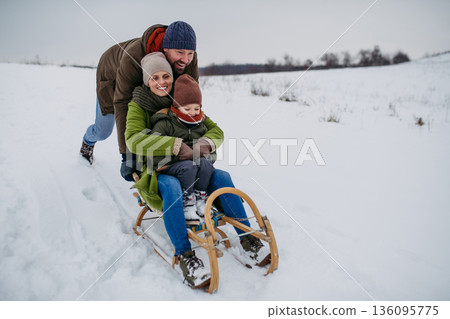 Winter family adventure with parents and little son sledding. Winter family adventure with parents and little son sledding. 136095775