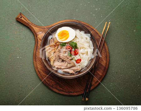 Asian soup rice noodles duck meat egg chopsticks ramen bowl green rustic background Asian soup rice noodles duck meat egg chopsticks ramen bowl green rustic background 136095786