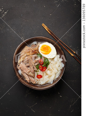 Asian soup rice noodles duck meat egg chopsticks ramen bowl dark rustic background Asian soup rice noodles duck meat egg chopsticks ramen bowl dark rustic background 136095789