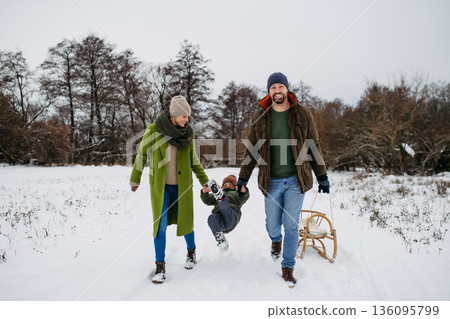Parents and little son on walk in winter forest, during snowfall. Parents and little son on walk in winter forest, during snowfall. 136095799