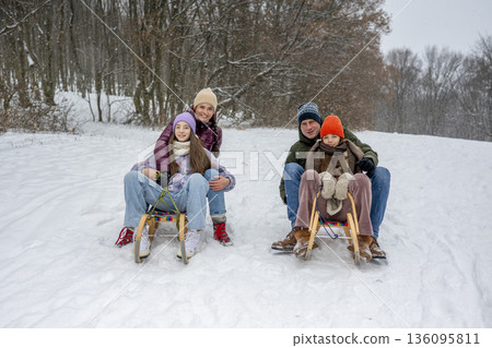 Family enjoying winter sledding together on snowy hill. Family enjoying winter sledding together on snowy hill. 136095811