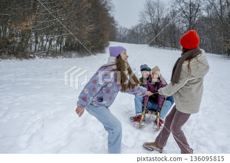 Family enjoying winter sledding together on snowy hill. 136095815