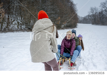 Family enjoying sledding in nature, pulling n sled through winter landscape. 136095816