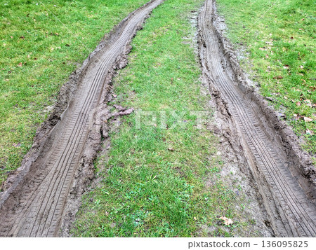 Close Up of Muddy Thick Mud Tire Wheel Tracks on a Country Road Travelling Through Grass and Field. Close Up of Muddy Thick Mud Tire Wheel Tracks on a Country Road Travelling Through Grass and Field. 136095825