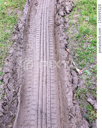 Close Up of Muddy Thick Mud Tire Wheel Tracks on a Country Road Travelling Through Grass and Field. 136095828