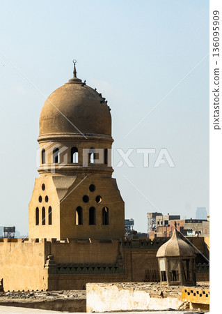 A historic mosque in Egypt with a prominent dome and intricate architectural details. Surrounding buildings are visible in the background under a clear blue sky. A historic mosque in Egypt with a prominent dome and intricate architectural details. Surrounding buildings are visible in the background under a clear blue sky. 136095909