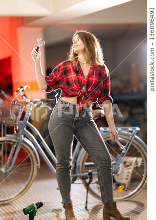 Woman holding wrenches repairing bicycle in workshop 136096491