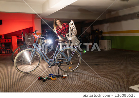 Woman installing child seat on bicycle preparing for family ride 136096525