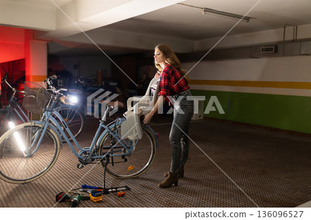 Woman attaching child seat to bicycle in garage 136096527