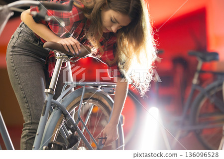 Young woman repairing bicycle wheel in bike workshop Young woman repairing bicycle wheel in bike workshop 136096528