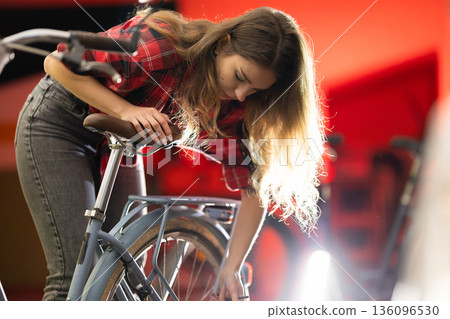 Young woman repairing bicycle wheel in workshop Young woman repairing bicycle wheel in workshop 136096530