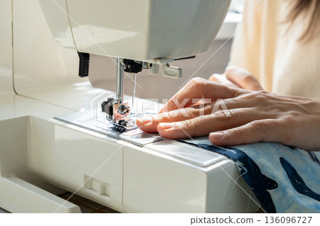 person sews product made blue fabric on sewing machine. tailor focused on work, calm relaxed mood. person sews product made blue fabric on sewing machine. tailor focused on work, calm relaxed mood. 136096727