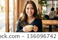 一位面帶微笑的日本女子在咖啡館欣賞著拉花咖啡，嘴唇上還沾著奶泡。 136096742