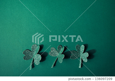 Three glittering shamrocks creating festive border on vibrant green background 136097209