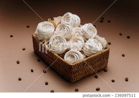 White meringue rosettes in wicker basket with coffee beans, beige copy space White meringue rosettes in wicker basket with coffee beans, beige copy space 136097511