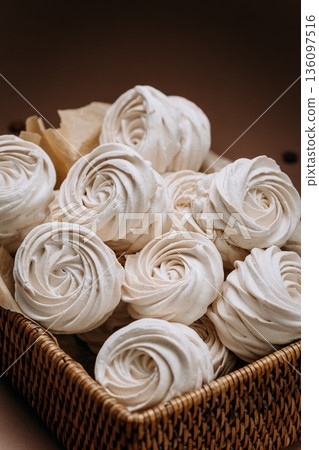 Wicker basket of white meringue rosettes on beige background, close up 136097516