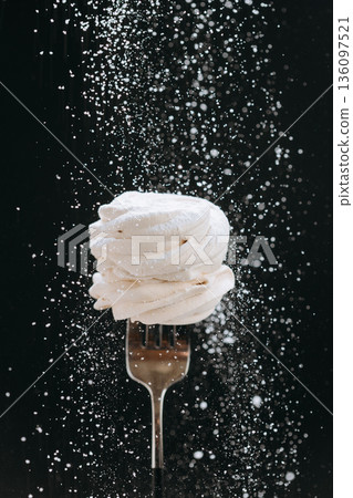 Powdered sugar falling over vanilla meringue on fork, black background 136097521