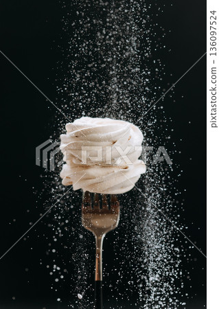 Powdered sugar falling over vanilla meringue on fork, black background Powdered sugar falling over vanilla meringue on fork, black background 136097524