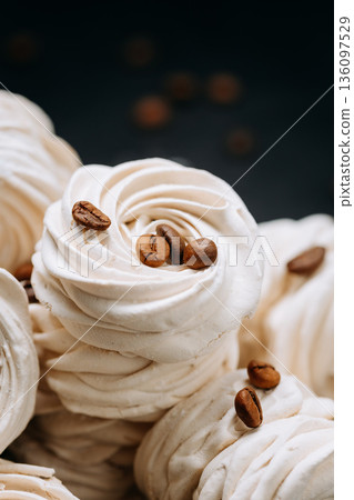 Macro of white meringue swirls topped with coffee beans on dark background 136097529