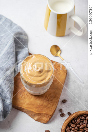 Iced Dalgona coffee on a wooden board on a gray concrete background with milk jug 136097594