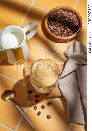 Dalgona coffee on a kitchen orange tile background with milk jug, coffee beans and morning shadow Dalgona coffee on a kitchen orange tile background with milk jug, coffee beans and morning shadow 136097595