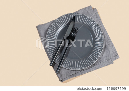 A ceramic dark gray plate with a black cutlery and napkin on a yellow isolated background. A ceramic dark gray plate with a black cutlery and napkin on a yellow isolated background. 136097599