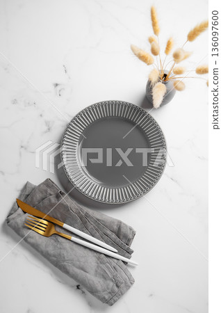 A ceramic gray plate with a cutlery, linen napkin and dry flowers bouquet on a marble background. A ceramic gray plate with a cutlery, linen napkin and dry flowers bouquet on a marble background. 136097600
