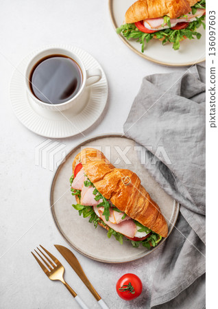 Croissant sandwich with ham, mozarella cheese, tomato, arugula on a plate and cup of coffee Croissant sandwich with ham, mozarella cheese, tomato, arugula on a plate and cup of coffee 136097603