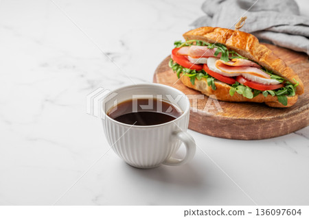 Croissant sandwich with ham, mozarella cheese, tomato, arugula on a wooden board and cup of coffee Croissant sandwich with ham, mozarella cheese, tomato, arugula on a wooden board and cup of coffee 136097604
