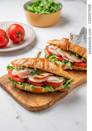 Two croissant sandwiches with ham, mozarella cheese and arugula on a wooden board 136097606