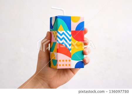 Hand Holding Bright Colorful Juice Box with Straw on Clean Background Hand Holding Bright Colorful Juice Box with Straw on Clean Background 136097780