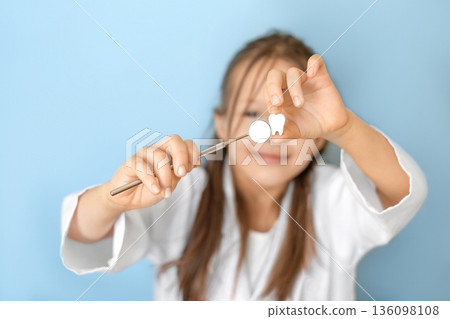 Child holding dental mirror and tooth model on blue background. Concept of pediatric dentistry, oral hygiene, healthy teeth, dental care, prevention and children healthcare. 136098108